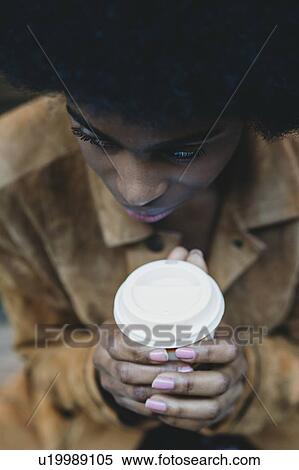Stock Photography - Young woman with afro hair clasping hot drink. Fotosearch
