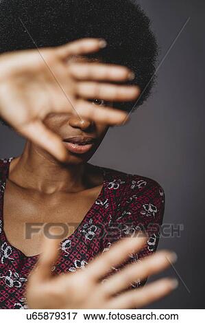 Stock Photo - Young woman with afro hair covering face with hands, grey background. Fotosearch