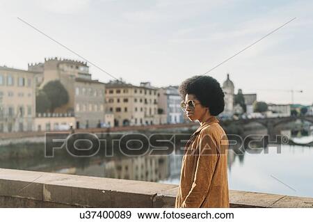 Stock Photo - Young woman with afro hair crossing bridge, Florence, Toscana, Italy. Fotosearch