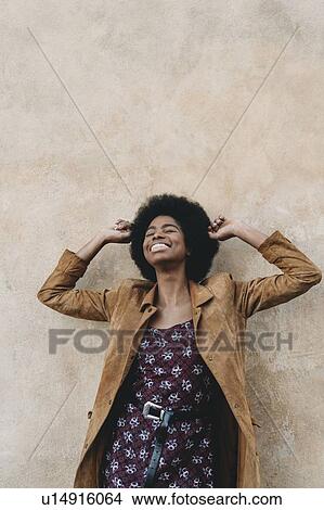 Young woman with afro hair feeling excited against stone wall View Large Photo Image Picture - Young woman with afro hair feeling excited against stone wall. Fotosearch
