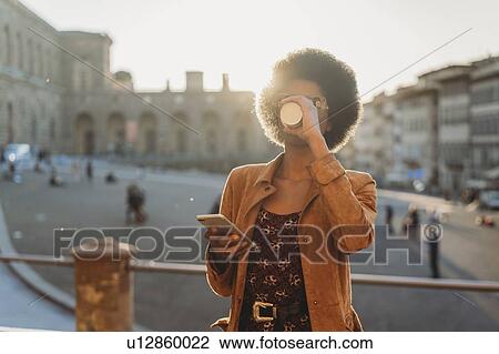 Young woman with afro hair having hot drink, using smartphone in city, Florence, Toscana, Italy View Large Photo Image Stock Image - Young woman with afro hair having hot drink, using smartphone in city, Florence, Toscana, Italy. Fotosearch