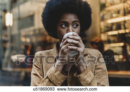Stock Image - Young woman with afro hair having hot drink in front of cafe. Fotosearch