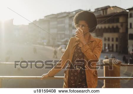 Stock Photo - Young woman with afro hair having hot drink in city, Florence, Toscana, Italy. Fotosearch