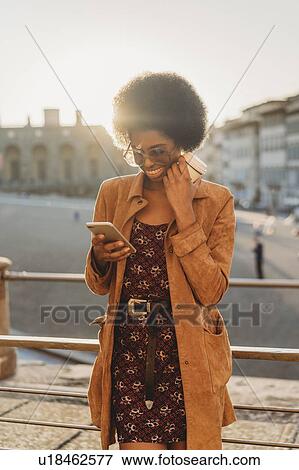 Young woman with afro hair having hot drink, using smartphone in city, Florence, Toscana, Italy View Large Photo Image Stock Photo - Young woman with afro hair having hot drink, using smartphone in city, Florence, Toscana, Italy. Fotosearch