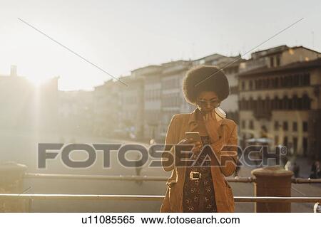 Young woman with afro hair having hot drink, using smartphone in city, Florence, Toscana, Italy View Large Photo Image Stock Photography - Young woman with afro hair having hot drink, using smartphone in city, Florence, Toscana, Italy. Fotosearch