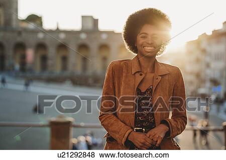 Stock Photo - Young woman with afro hair leaning against handrail, Florence, Toscana, Italy. Fotosearch