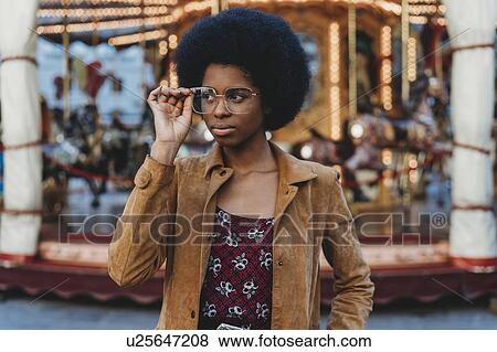 Young woman with afro hair putting on spectacles in front of carousel View Large Photo Image Stock Photo - Young woman with afro hair putting on spectacles in front of carousel. Fotosearch