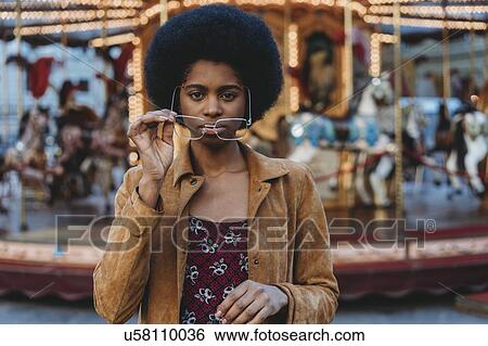 Young woman with afro hair putting on spectacles in front of carousel View Large Photo Image Stock Photograph - Young woman with afro hair putting on spectacles in front of carousel. Fotosearch