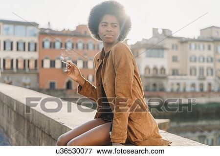 Young woman with afro hair smoking on bridge, Florence, Toscana, Italy View Large Photo Image Stock Photo - Young woman with afro hair smoking on bridge, Florence, Toscana, Italy. Fotosearch