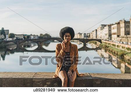 Stock Photo - Young woman with afro hair smoking on bridge, Florence, Toscana, Italy. Fotosearch