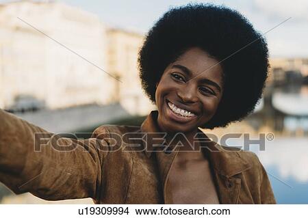Young woman with afro hair taking selfie in city View Large Photo Image Picture - Young woman with afro hair taking selfie in city. Fotosearch