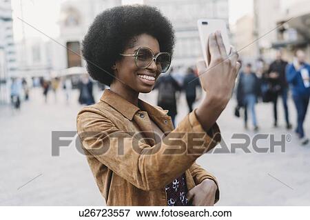 Young woman with afro hair taking selfie in city View Large Photo Image Stock Photo - Young woman with afro hair taking selfie in city. Fotosearch