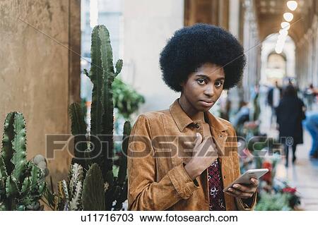 Young woman with afro hair using smartphone in city View Large Photo Image Stock Image - Young woman with afro hair using smartphone in city. Fotosearch