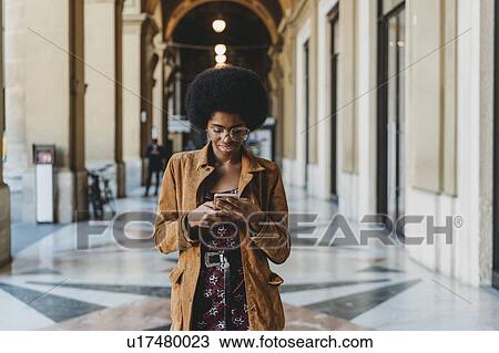 Young woman with afro hair using smartphone in building corridor View Large Photo Image Stock Image - Young woman with afro hair using smartphone in building corridor. Fotosearch