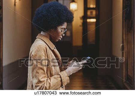 Young woman with afro hair using smartphone in front of building View Large Photo Image Stock Image - Young woman with afro hair using smartphone in front of building. Fotosearch