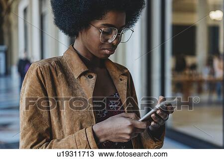 Young woman with afro hair using smartphone in building corridor View Large Photo Image Stock Image - Young woman with afro hair using smartphone in building corridor. Fotosearch
