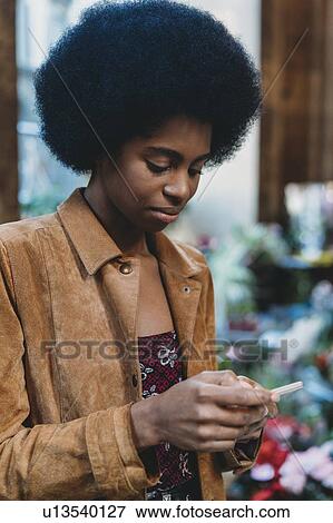 Stock Photo - Young woman with afro hair using smartphone in city. Fotosearch
