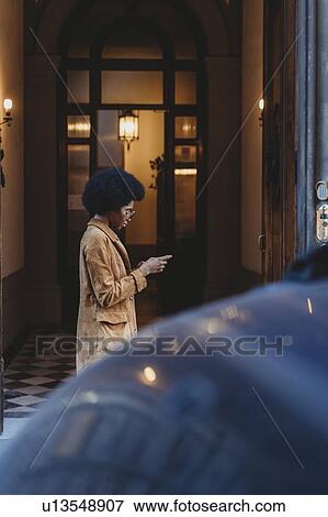 Young woman with afro hair using smartphone in front of building View Large Photo Image Stock Photo - Young woman with afro hair using smartphone in front of building. Fotosearch