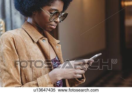 Young woman with afro hair using smartphone in front of building View Large Photo Image Stock Photography - Young woman with afro hair using smartphone in front of building. Fotosearch