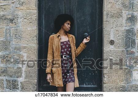 Picture - Young woman with afro hair waiting at door of stone building. Fotosearch
