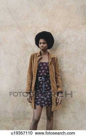 Stock Image - Young woman with afro hair waiting against stone wall. Fotosearch