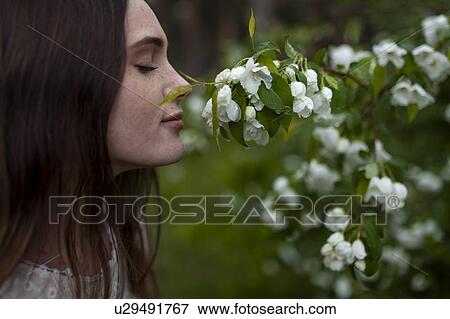 Stock Photo - Young woman with her eyes closed sniffing flowers. Fotosearch