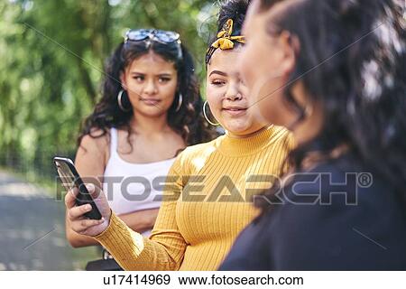 Young woman with teenage sisters looking at smartphone by park, over shoulder view View Large Photo Image Stock Photo - Young woman with teenage sisters looking at smartphone by park, over shoulder view. Fotosearch