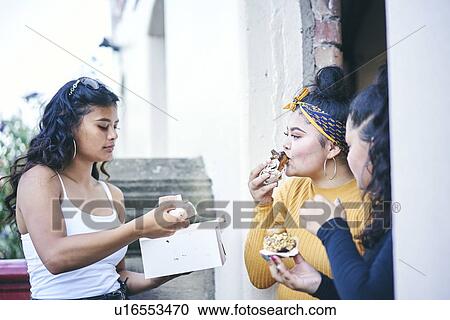Stock Image - Young woman with teenage sisters while eating cakes in doorway. Fotosearch