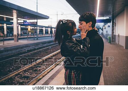 Stock Photograph - Affectionate young couple on train station platform, Milan, Italy. Fotosearch