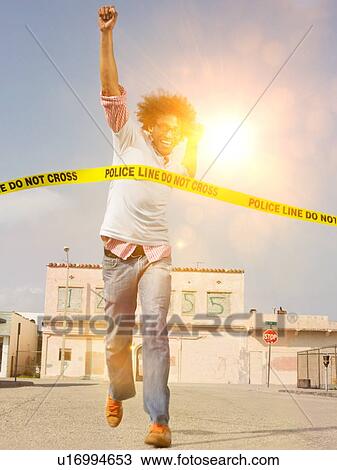 Stock Image - African American man smiling as he runs through police do not cross tape. Fotosearch