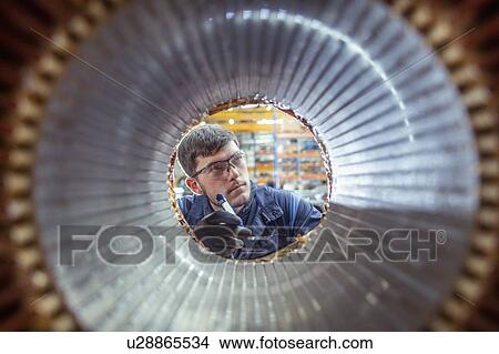 Picture - Apprentice electrical engineer inspecting winding on generator stator in electrical engineering factory. Fotosearch