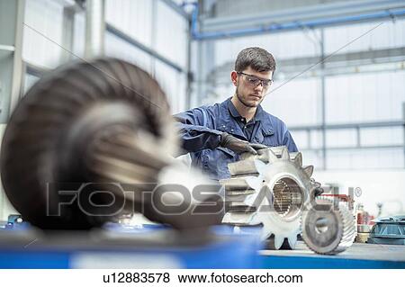 Apprentice engineer cleaning gear for pump in electrical engineering factory View Large Photo Image Stock Photo - Apprentice engineer cleaning gear for pump in electrical engineering factory. Fotosearch