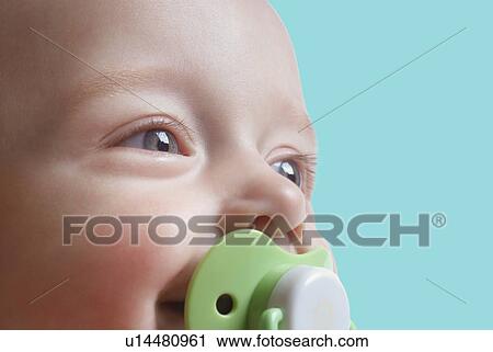 Stock Image - Baby boy with pacifier against blue background. Fotosearch