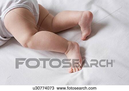 Stock Image - Baby lying on bed low section. Fotosearch