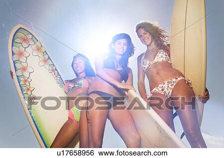 Stock Photograph - Beautiful Multi Ethnic Surfer Girls holding surfboards wearing bikinis. Fotosearch