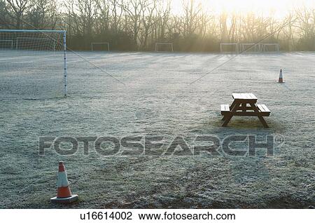Stock Image - Bench and bollards on empty soccer field at sunset. Fotosearch