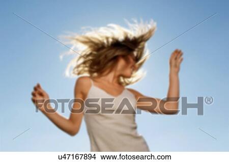Picture - Blurred image of woman swishing her hair outside. Fotosearch