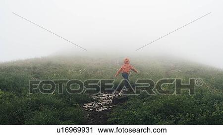 Stock Image - Boy hiking in thick fog on hilltop. Fotosearch
