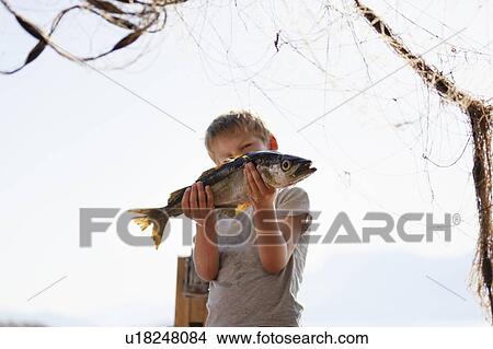Picture - Boy holding up fish, fishing net in foreground. Fotosearch