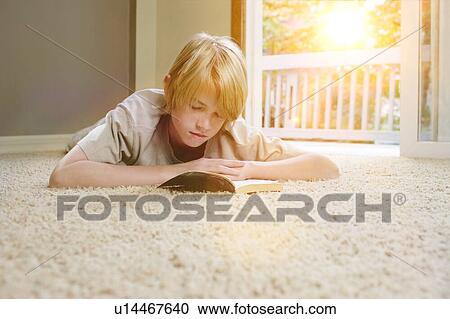 Stock Image - Boy lying on carpet, reading book. Fotosearch