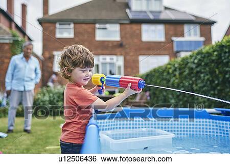 Boy playing with water gun by pool View Large Photo Image Stock Photograph - Boy playing with water gun by pool. Fotosearch