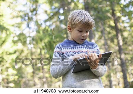 Stock Photo - Boy using digital tablet in forest. Fotosearch