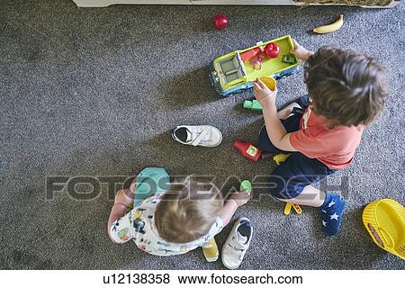 Stock Photo - Boys playing with toy trucks and assorted toys on rug. Fotosearch