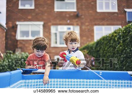 Stock Photography - Boys playing with water gun by pool. Fotosearch