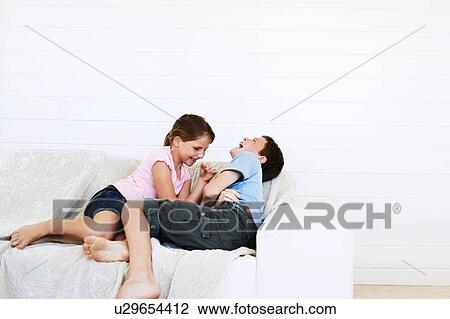 Stock Image - Brother and sister relaxing on sofa together. Fotosearch
