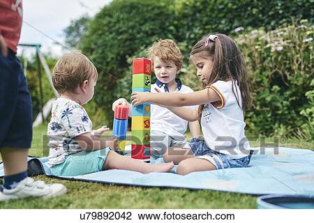 Stock Image - Brother and sisters playing with blocks on picnic blanket. Fotosearch