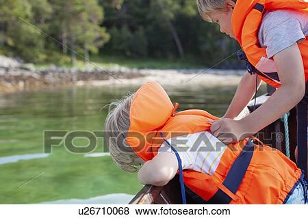 Stock Photo - Brothers looking into lake from boat, Norway. Fotosearch