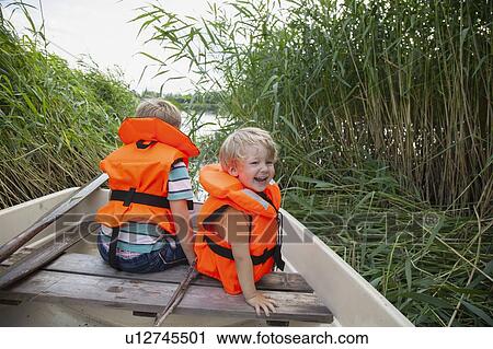 Stock Image - Brothers playing on boat moored in grass field. Fotosearch
