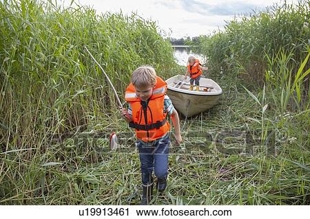 Stock Image - Brothers playing on boat moored in grass field. Fotosearch