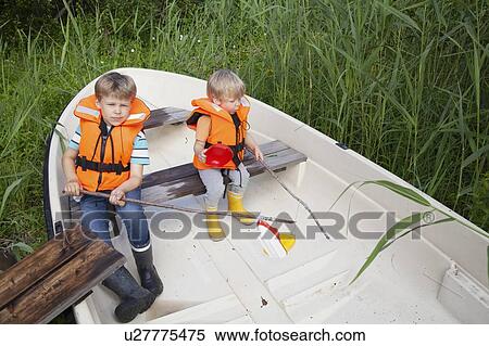 Stock Photography - Brothers playing on boat moored in grass field. Fotosearch